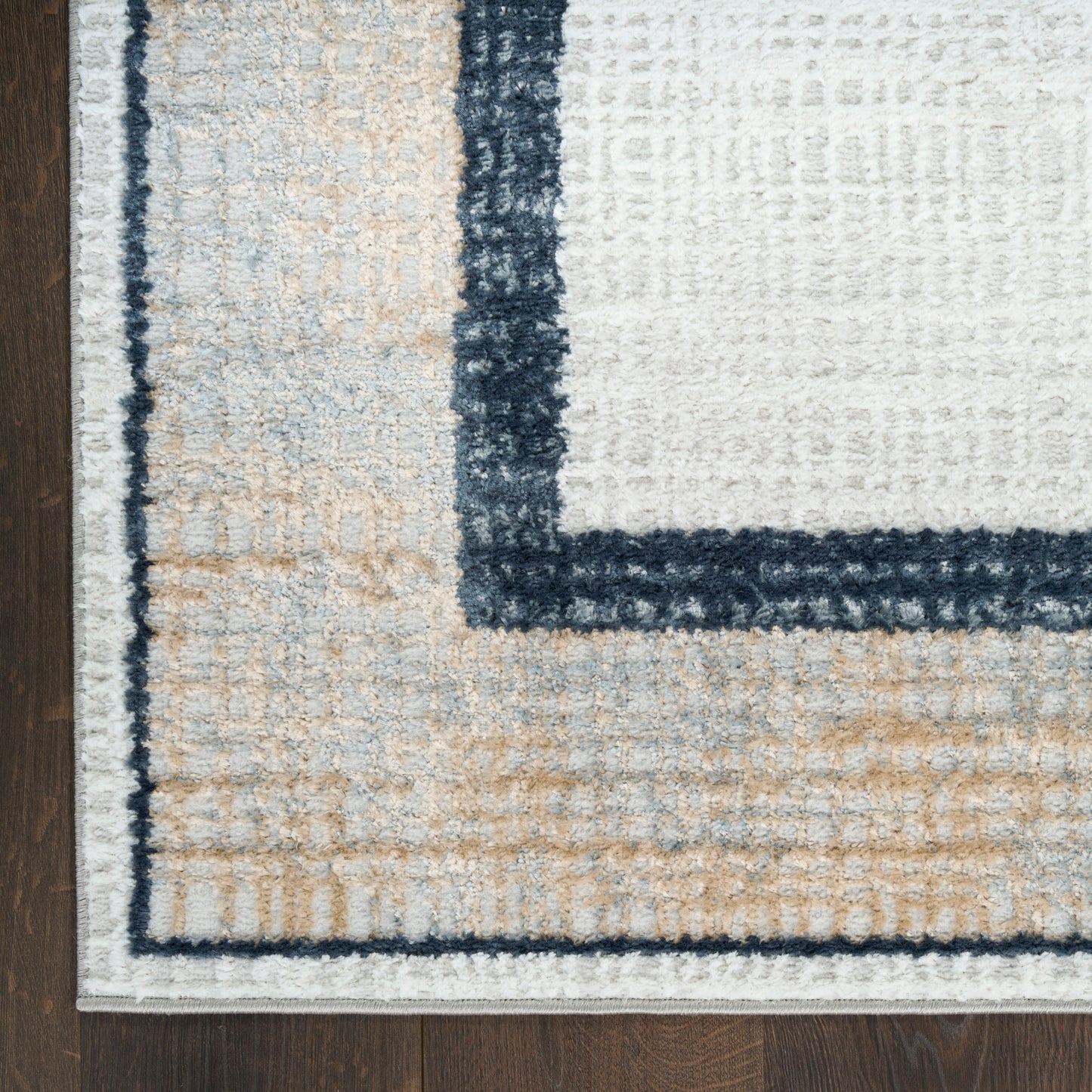 Textured beige and white area rug with a dark navy border on a wooden floor.