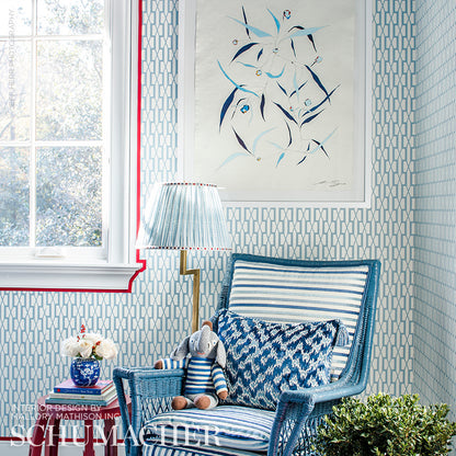 Blue geometric lattice wallpaper in a sunlit seating nook with striped wicker chair and brass lamp.