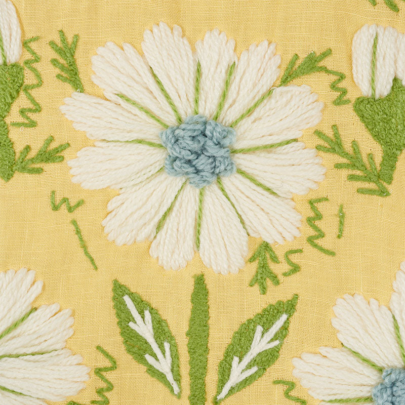 Embroidered white daisy petals with yellow centers on yellow woven fabric; green leaves and stems.