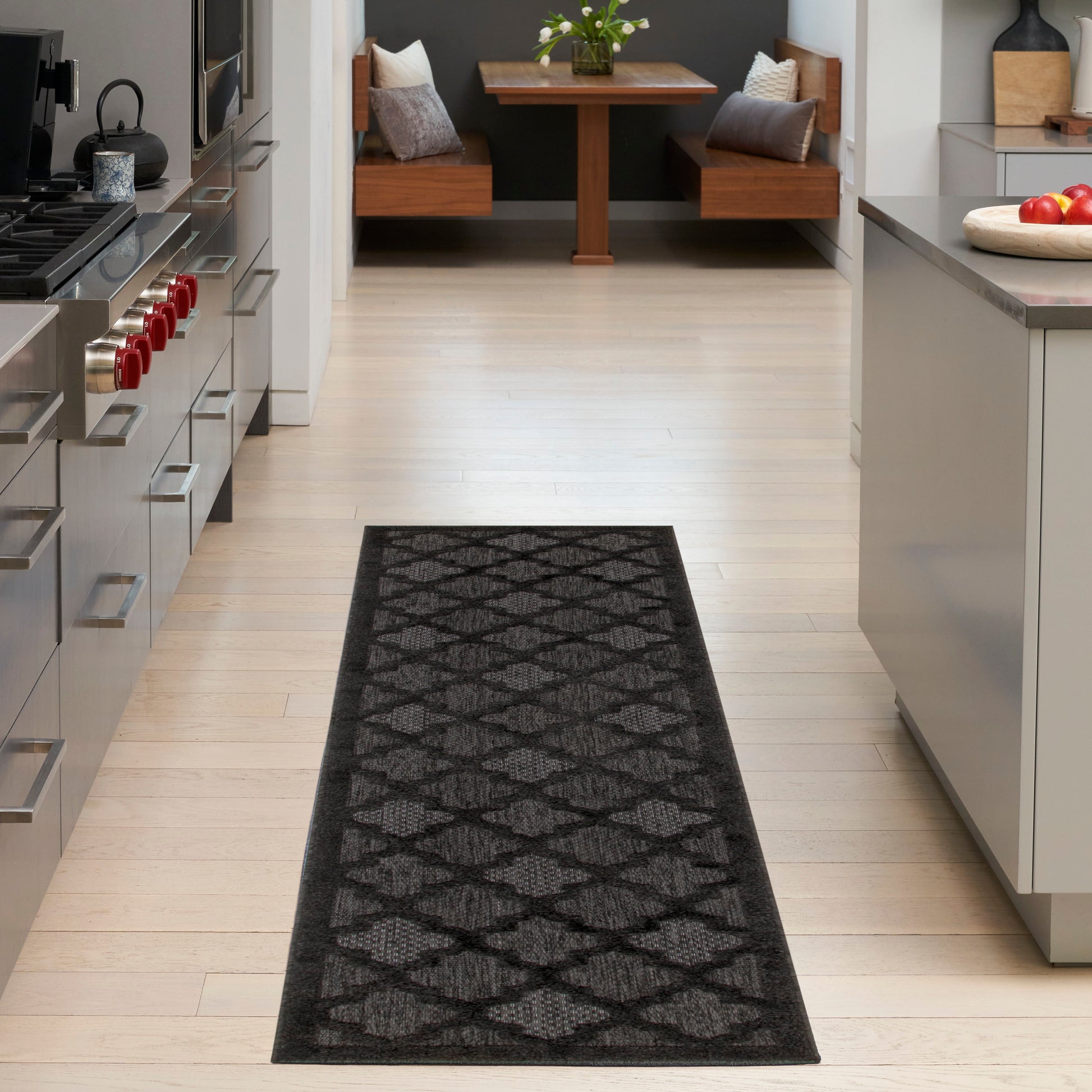Long charcoal runner rug with gray geometric diamond pattern on light wood floor in a modern kitchen.