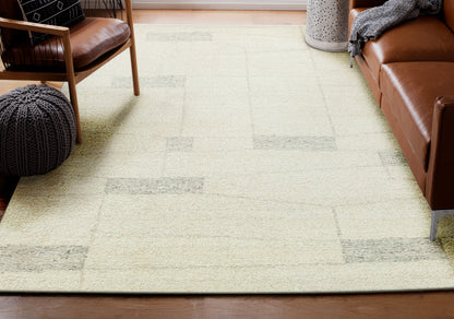 Beige geometric area rug with light gray rectangular blocks in a living room with brown leather sofa and knitted pouf.
