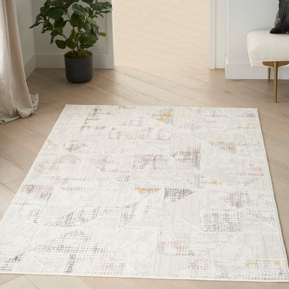 Soft neutral geometric patchwork area rug on light wood floor; cream, beige, gray with pale pink accents.