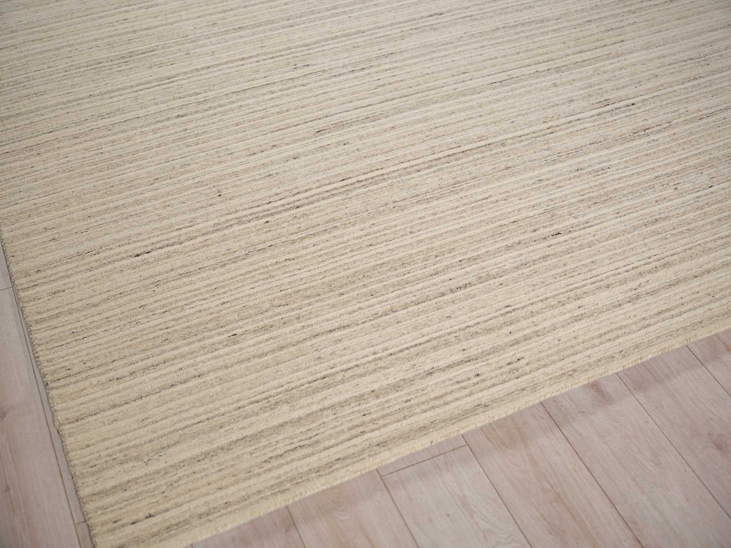 Beige area rug with thin cream and taupe horizontal stripes on a light wood floor