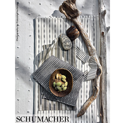Flat lay of gray striped textiles with a wooden bowl of pistachios, small stones, and a weathered driftwood branch.