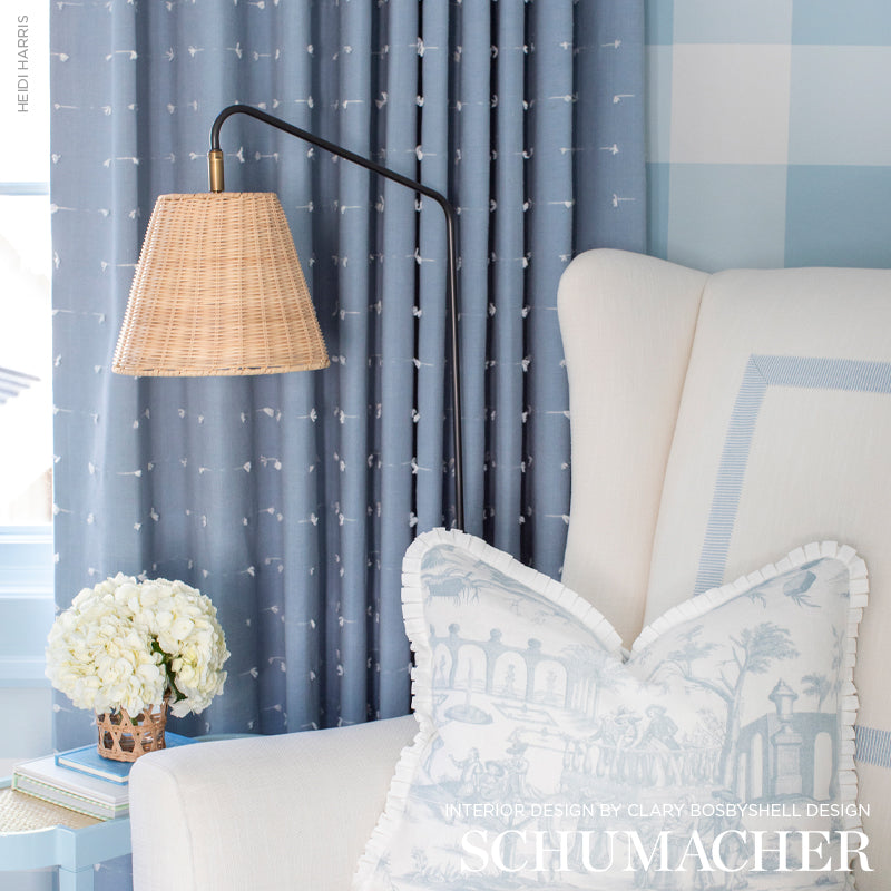 Blue living room corner with wicker shade floor lamp, pale tan chair, toile pillow, white hydrangea bouquet, blue curtains.