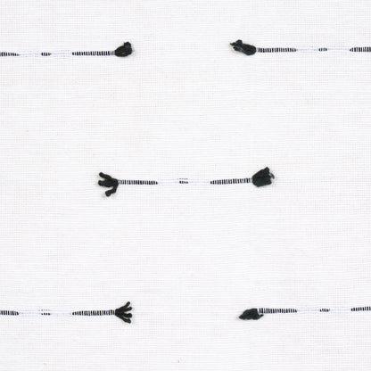 White fabric swatch with black-striped tassel trim cords laid horizontally; small black tassels at ends.