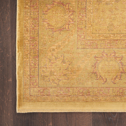 Golden yellow oriental rug with pink-toned border and floral medallions; fringed edge on dark hardwood floor.