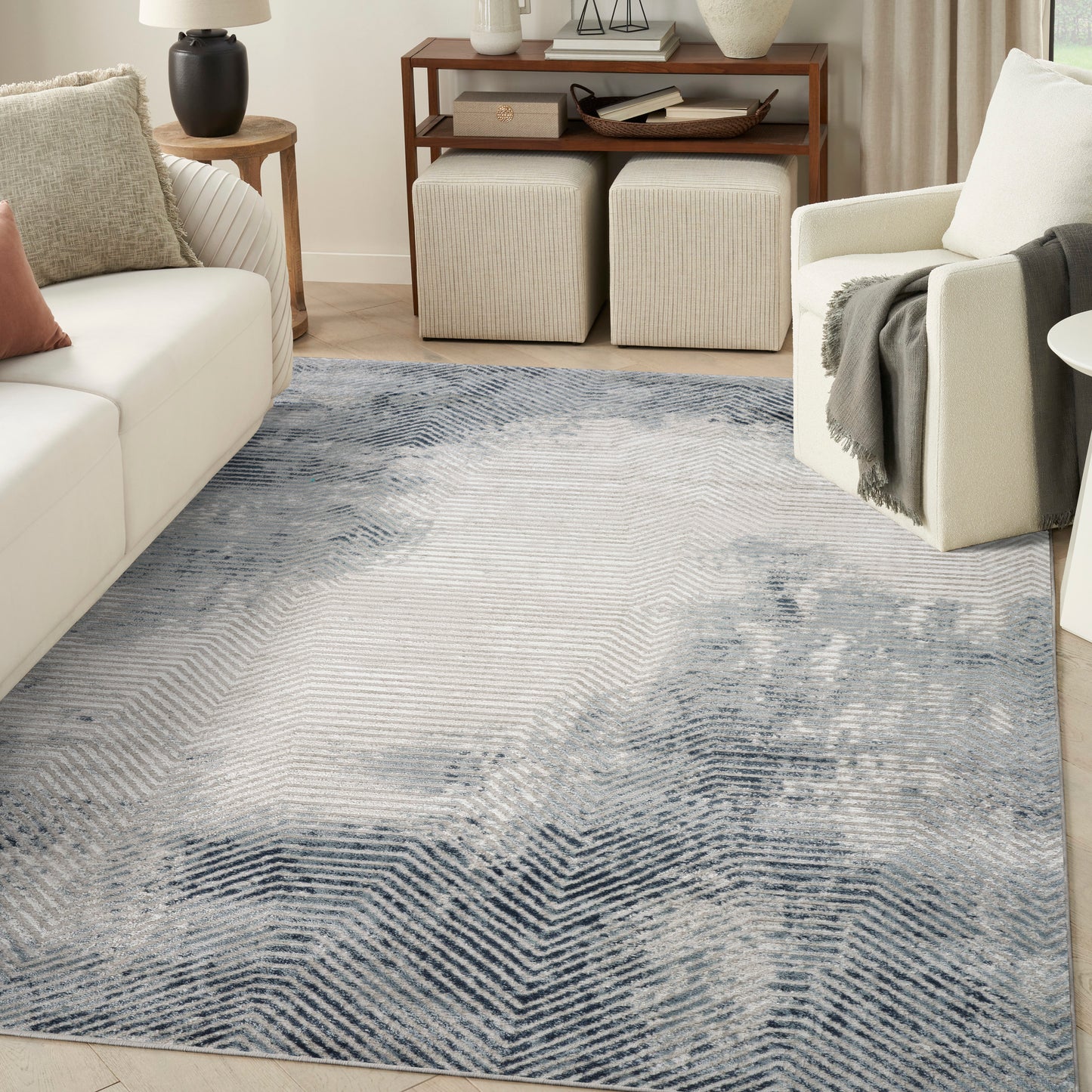 Blue & ivory chevron area rug in a bright living room with cream sofa, wood console, and beige ottomans.