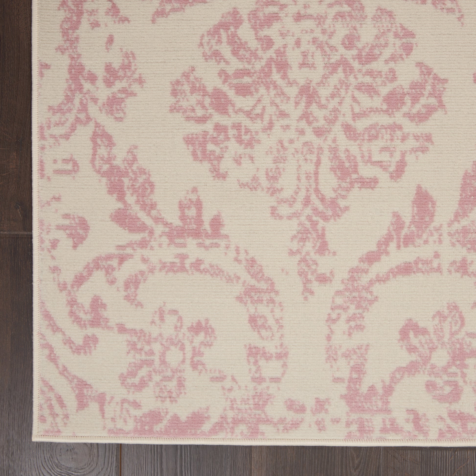 Rectangular area rug with cream/beige background and pink damask floral pattern; woven texture on wood floor.