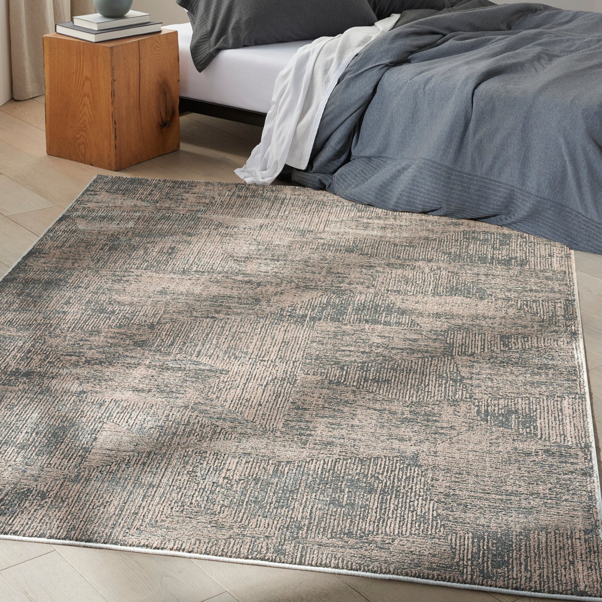 Neutral gray-beige geometric area rug on wood floor beside a bed with gray bedding and a wooden nightstand.