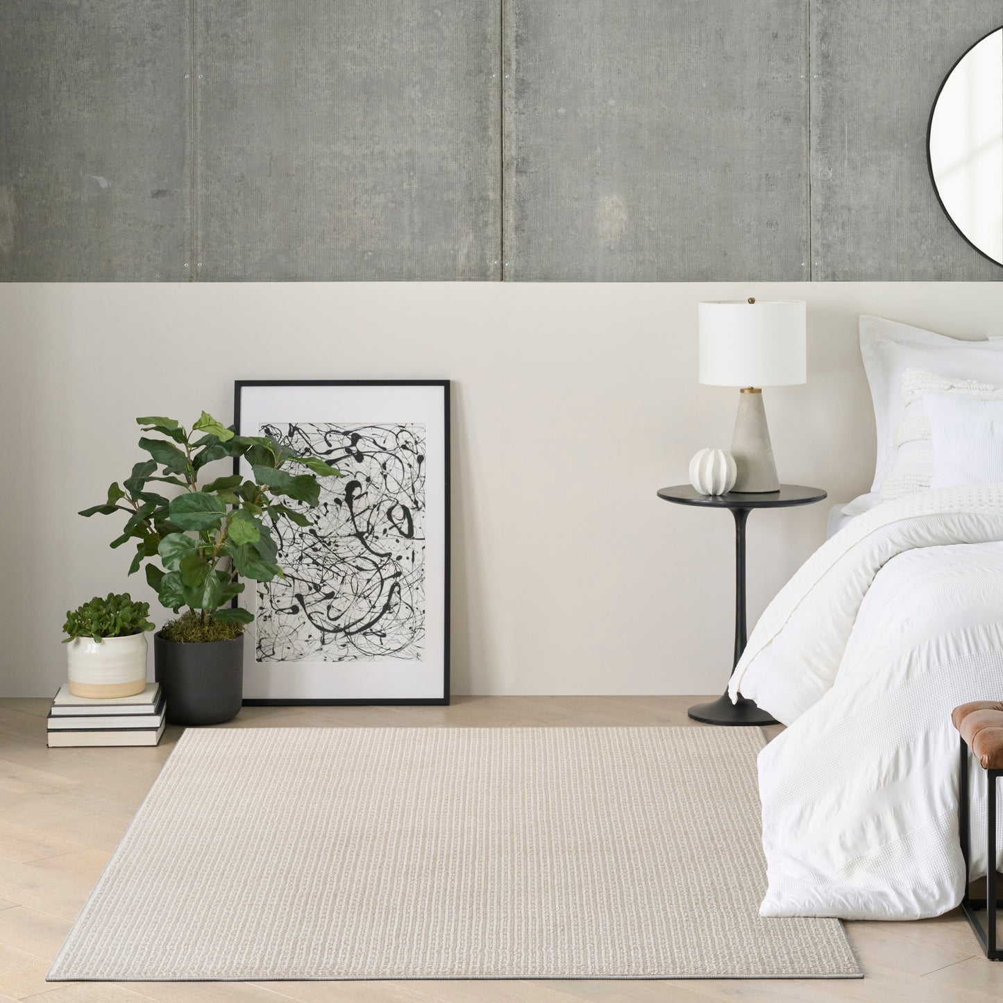 Modern bedroom corner with white bedding, black frame art, potted plant, beige rug, and side table with lamp.