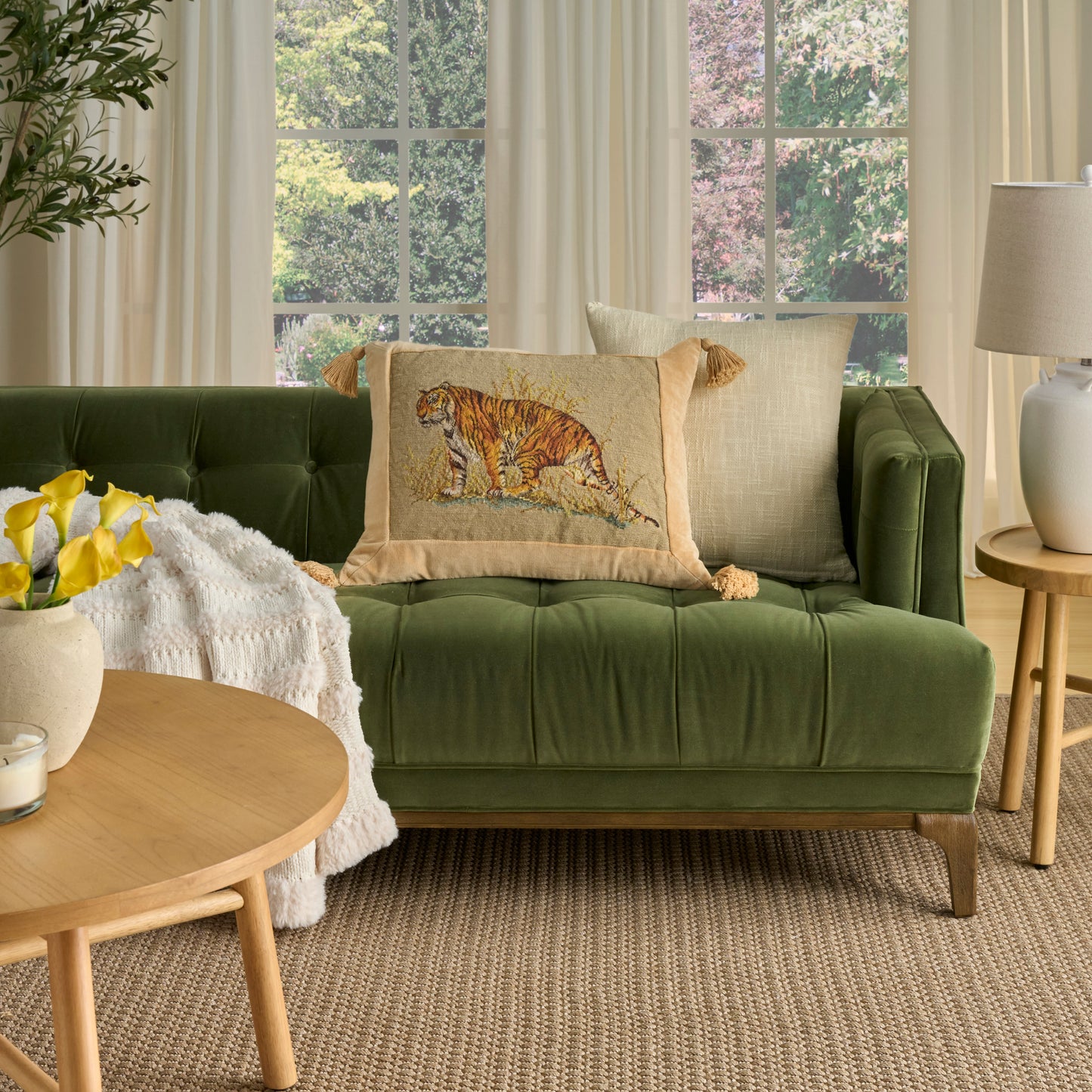 Green velvet sofa with tiger-print pillow, beige cushions, round wood coffee table, yellow flowers, white throw.