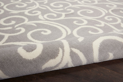 Soft gray area rug with white swirling scroll pattern, plush texture, edge folded on dark hardwood floor.