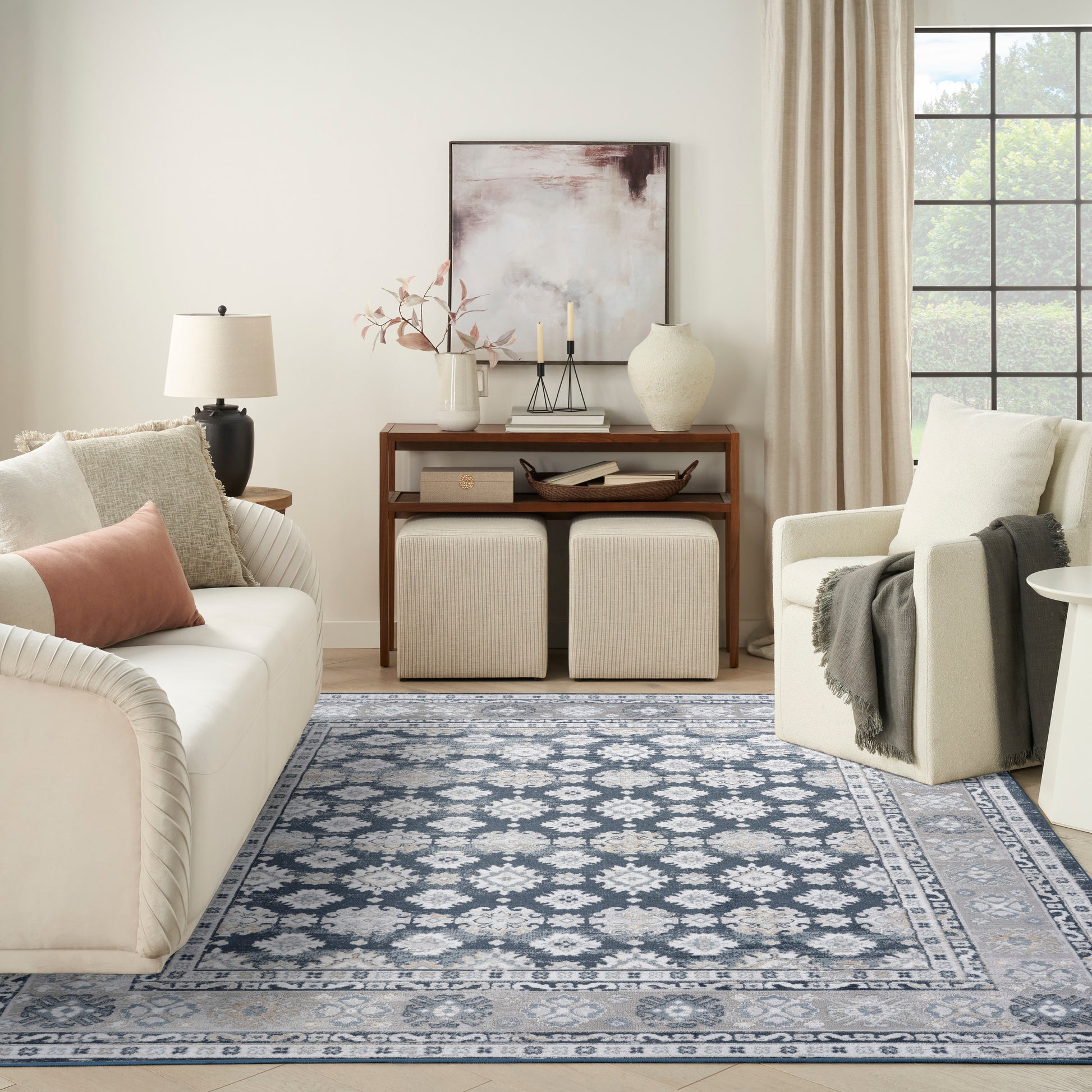 Blue and ivory geometric area rug anchors a neutral living room with cream sofa, ottomans, and a wooden console.