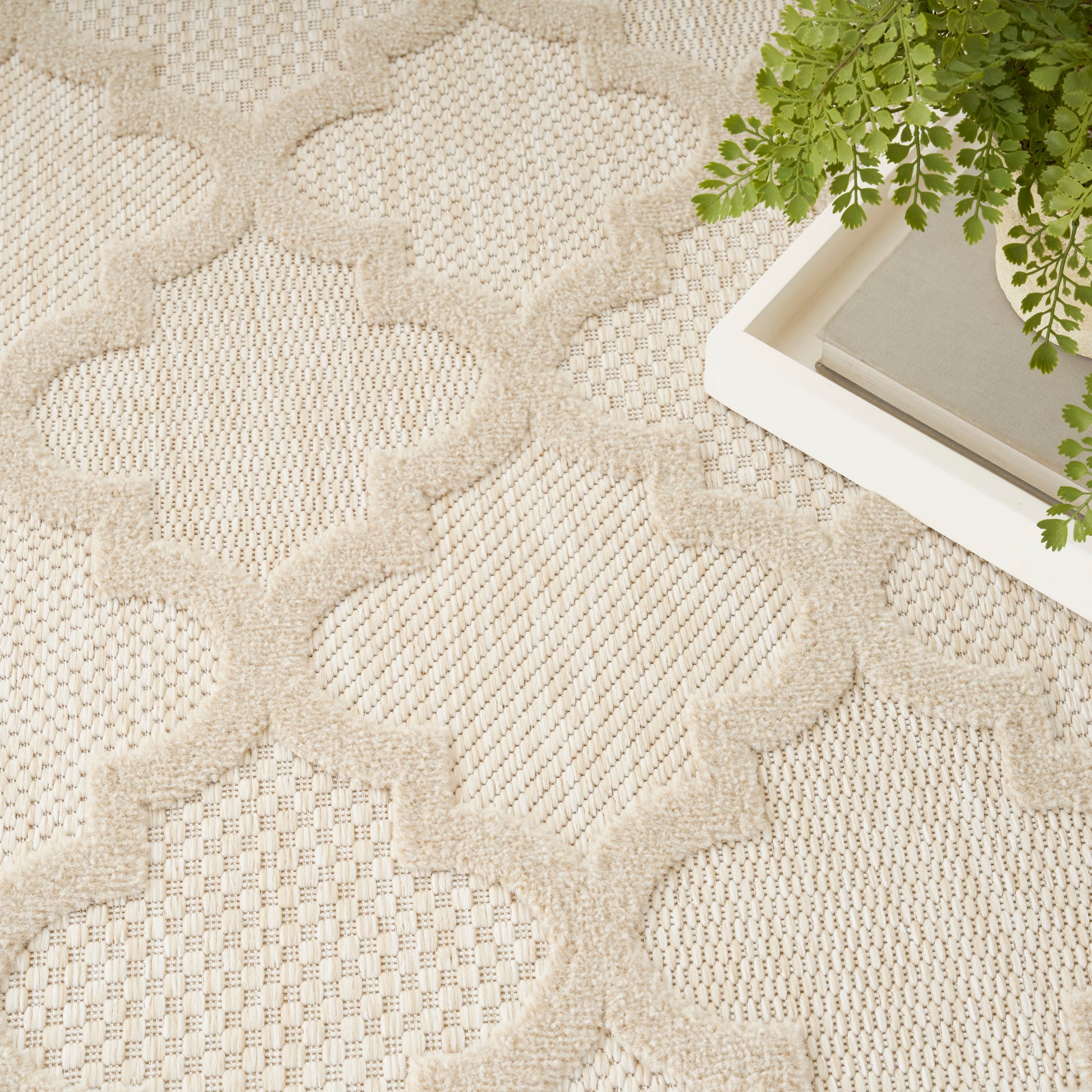 Beige tufted round area rug with geometric trellis pattern; plant in a white tray corner.
