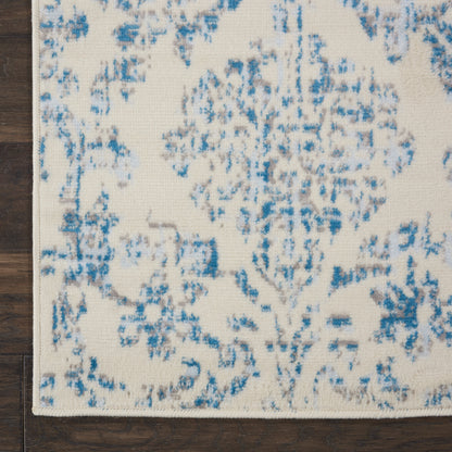 Cream woven rug with blue distressed damask pattern; ivory background, corner view on dark wood floor.
