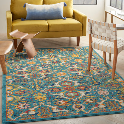 Vibrant teal, blue & yellow floral rug in a sunny living room with a mustard sofa & woven chairs.
