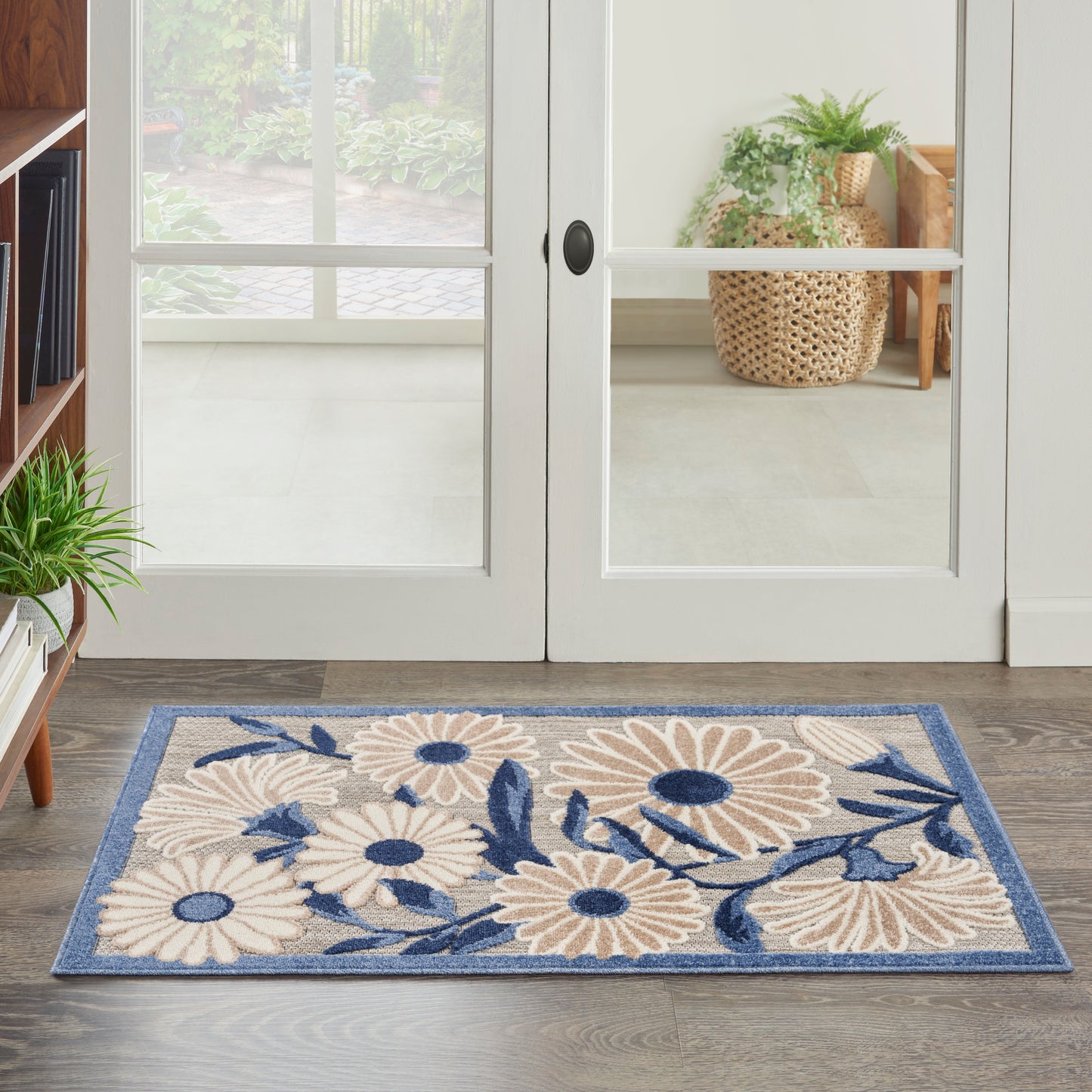 Rectangular area rug with beige daisies and blue leaves on a blue border, placed by glass doors.