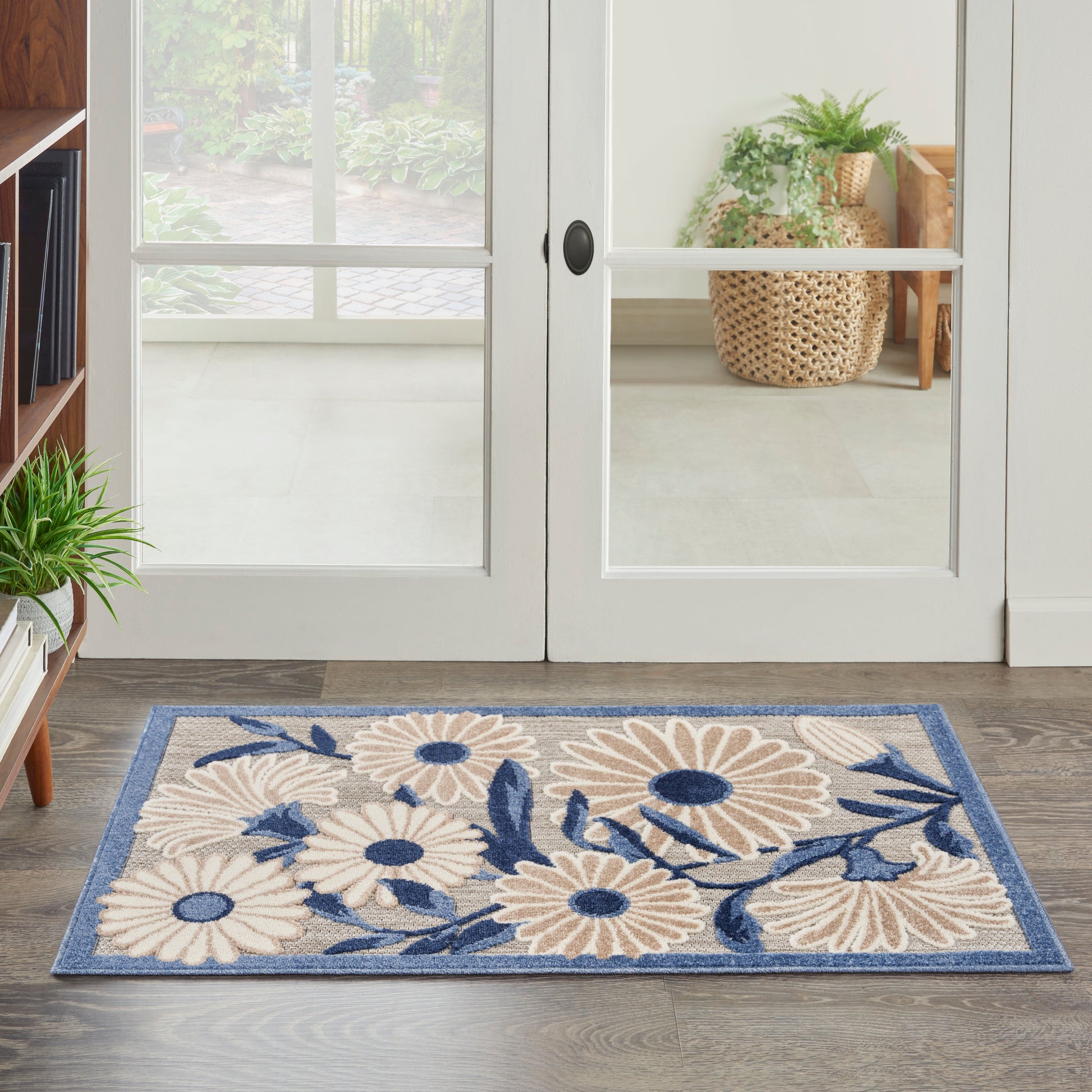 Rectangular area rug with beige daisies and blue leaves on a blue border, placed by glass doors.