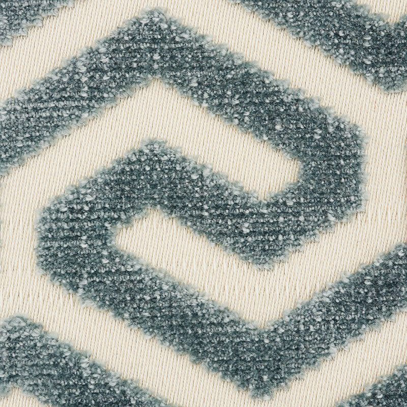 Close-up of a plush rug with blue-gray geometric diamond chevrons on cream background.