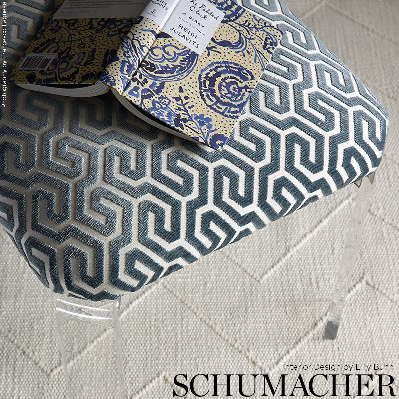 Blue-grey Greek-key patterned cushion on a beige quilted rug; fabric swatch resting on top.