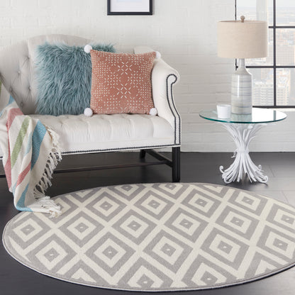 Round gray geometric rug under white tufted sofa with nailhead trim, blue faux-fur and pink pom-pom pillows, glass side table