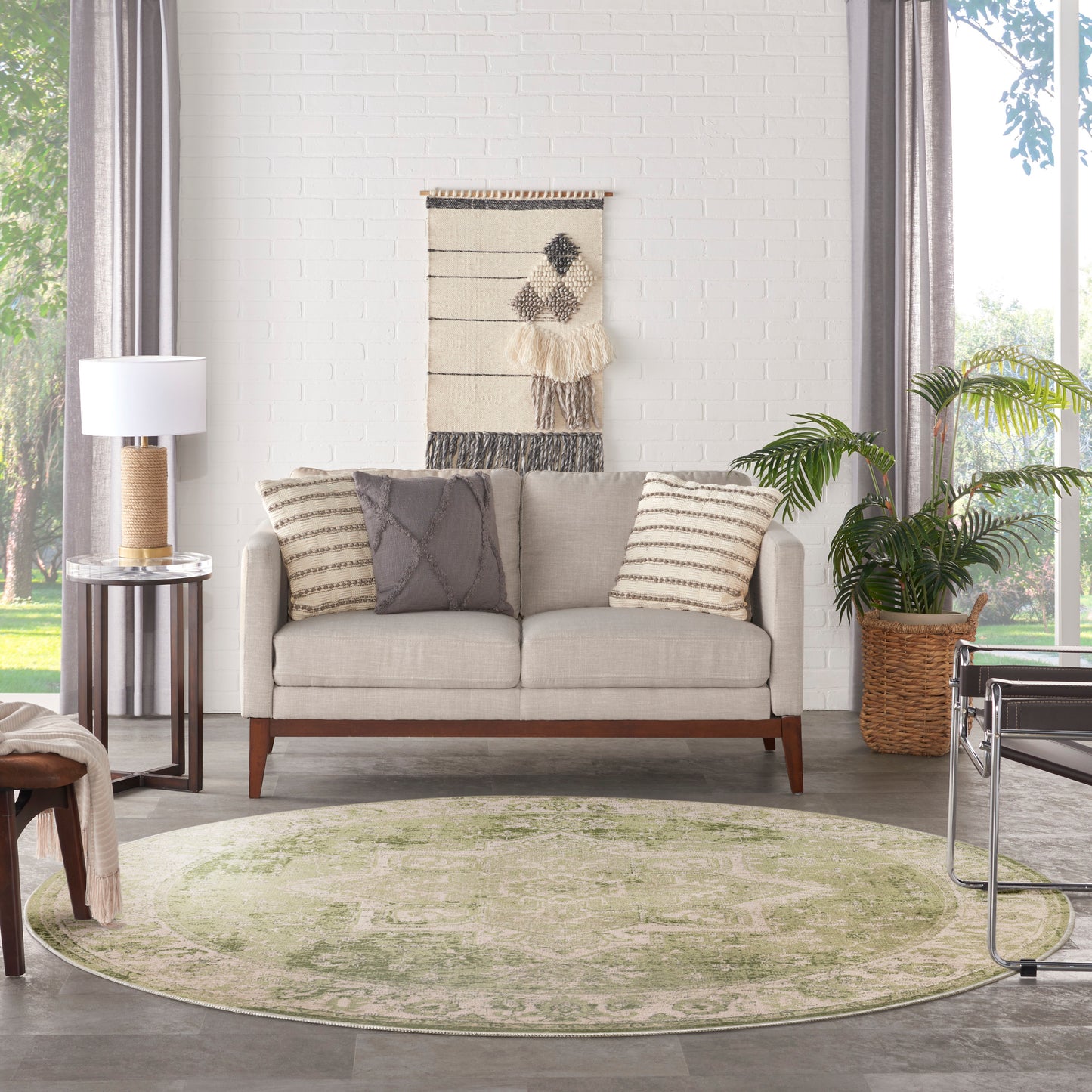 Beige mid-century sofa with striped and gray cushions, round pale-green rug, woven wall hanging, and potted plant.
