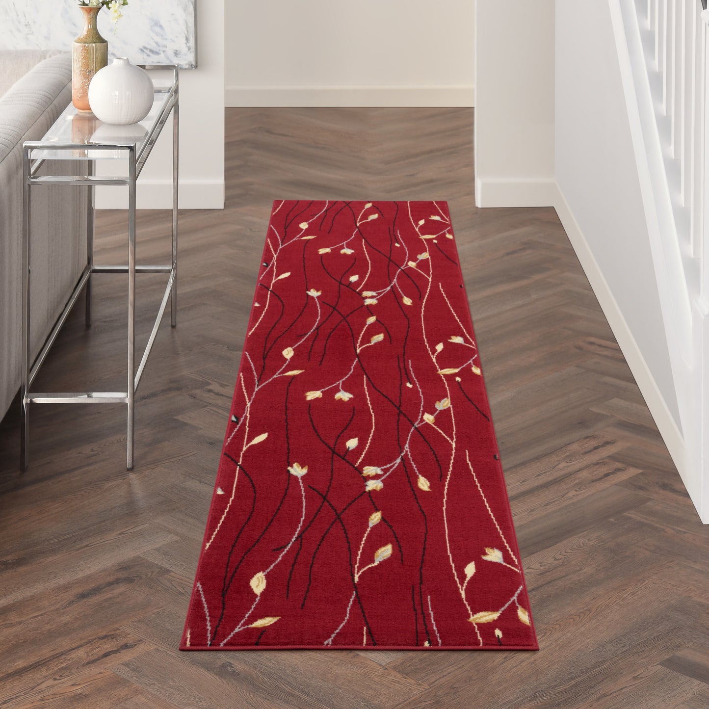 Red hallway runner rug with black vine pattern and cream leaves on dark wood floor.