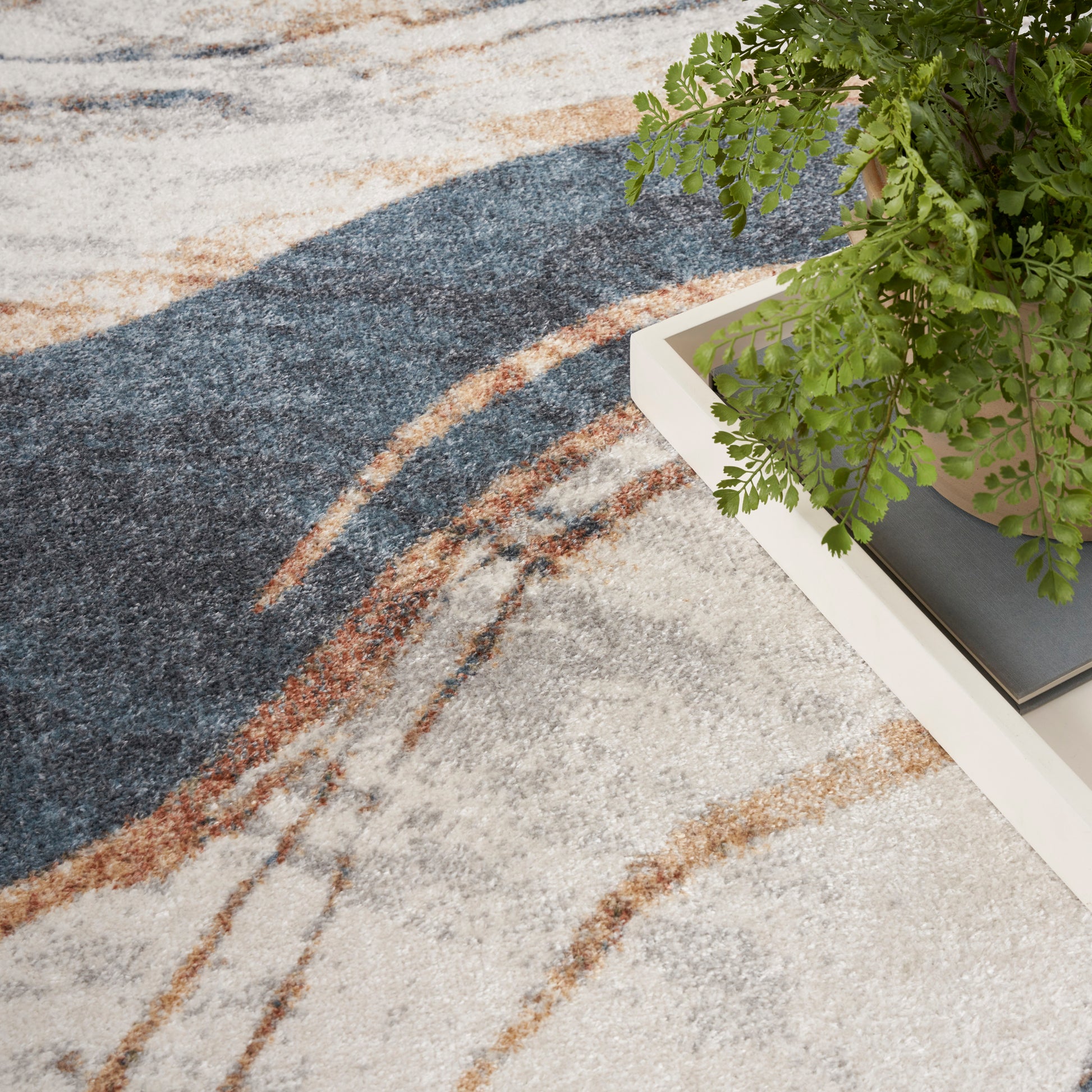 Abstract area rug with navy blue and tan curved lines on beige background beside a white coffee table and potted fern.