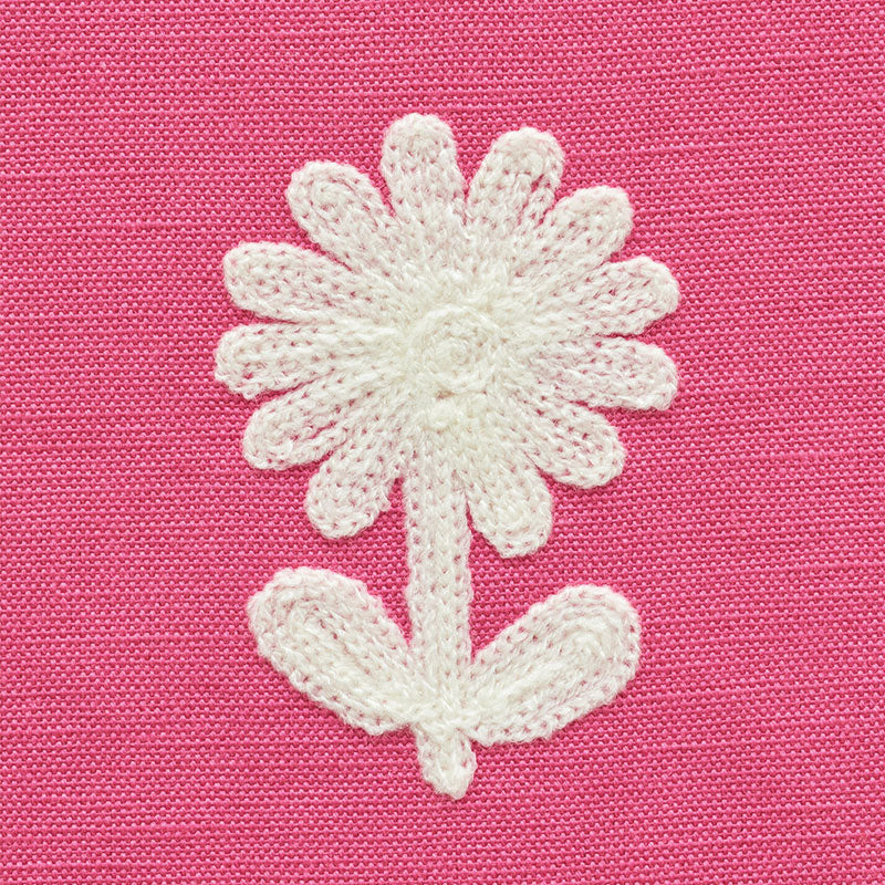 White embroidered daisy with stem and two leaves on pink textured fabric.