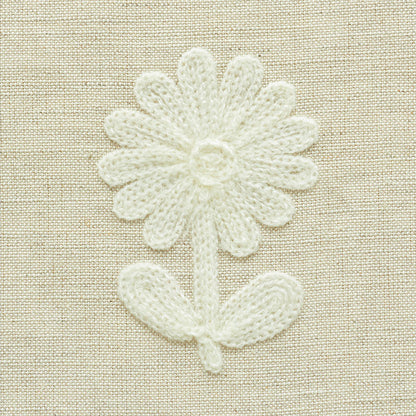 White crocheted daisy patch with stem and leaf on beige linen fabric.