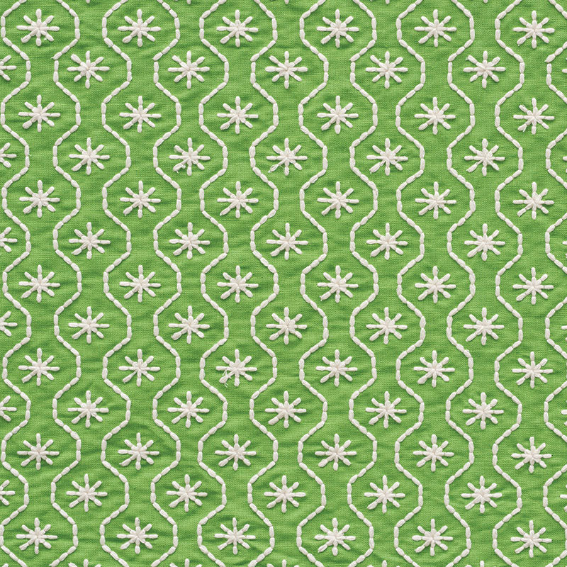 Green fabric with white embroidered interlocking loop trellis and starburst motifs.