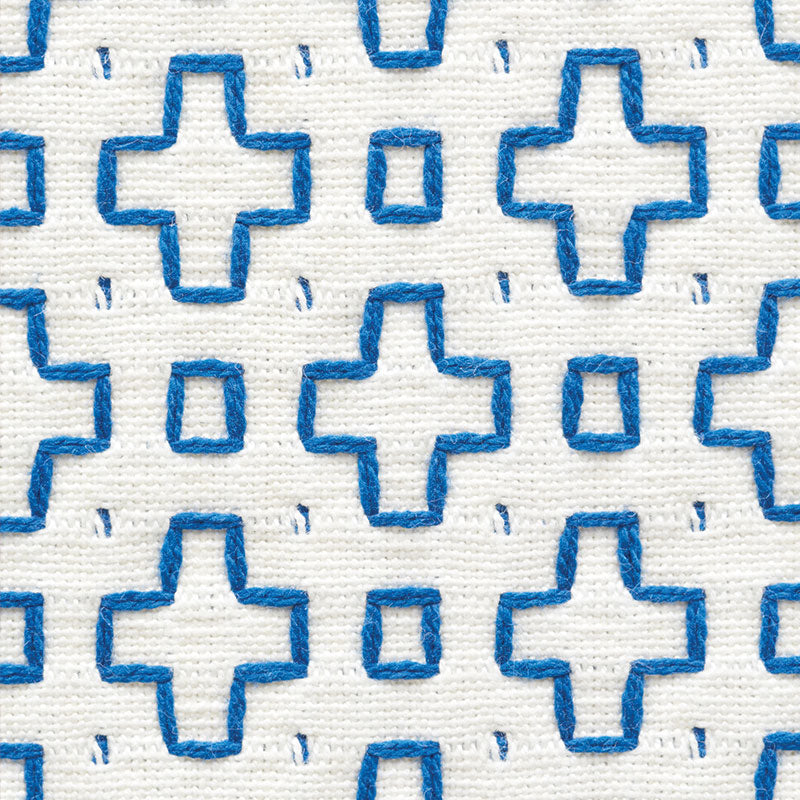 White fabric with repeating blue cross motifs and tiny square accents; textured embroidered pattern.