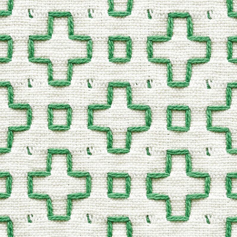 White fabric with green embroidered plus shapes and small squares; woven textile texture.