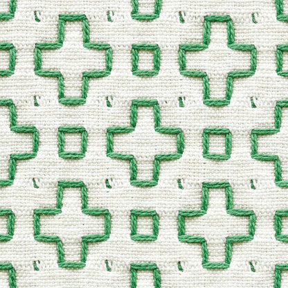 White fabric with green embroidered plus shapes and small squares; woven textile texture.