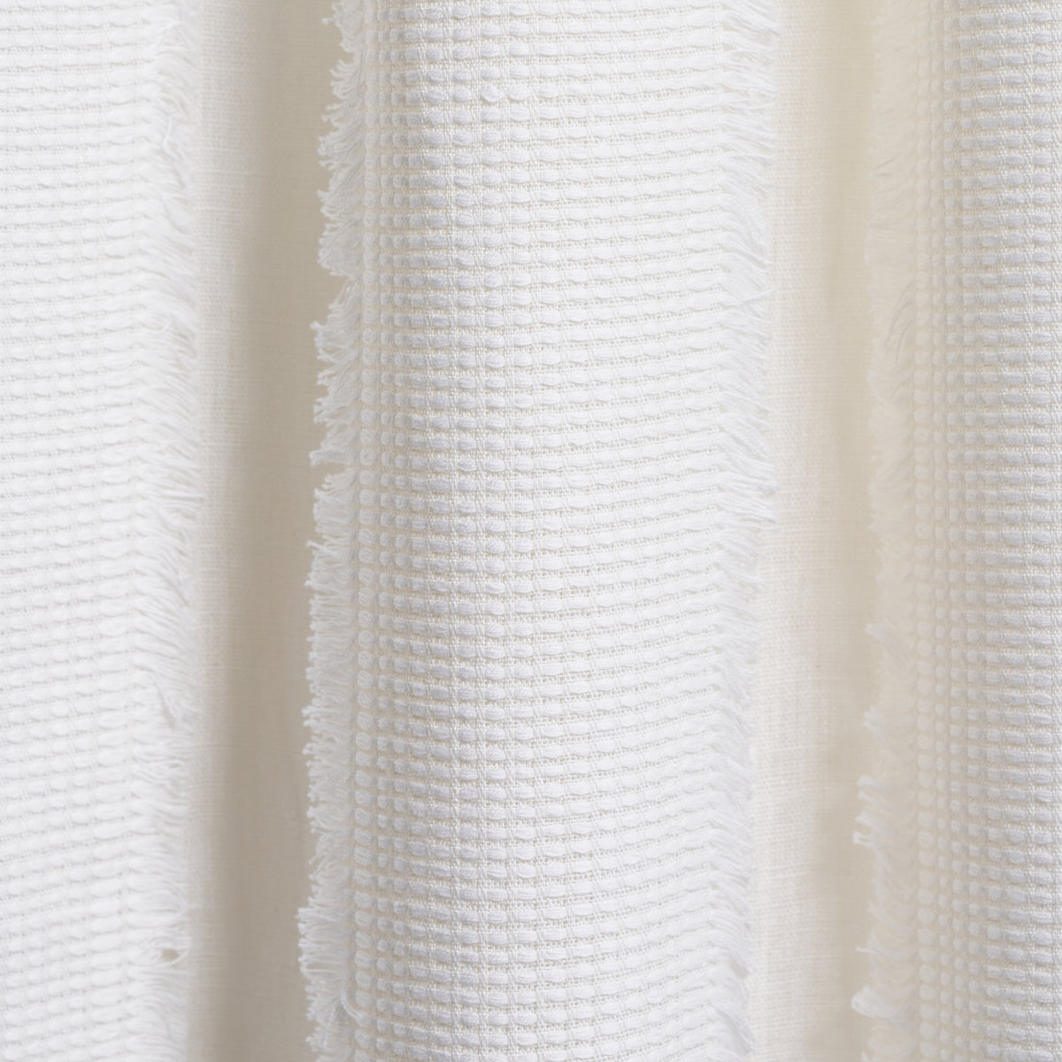 Close-up of white cotton towel fabric with waffle texture and fringed edges.