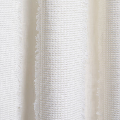Close-up of white cotton towel fabric with waffle texture and fringed edges.