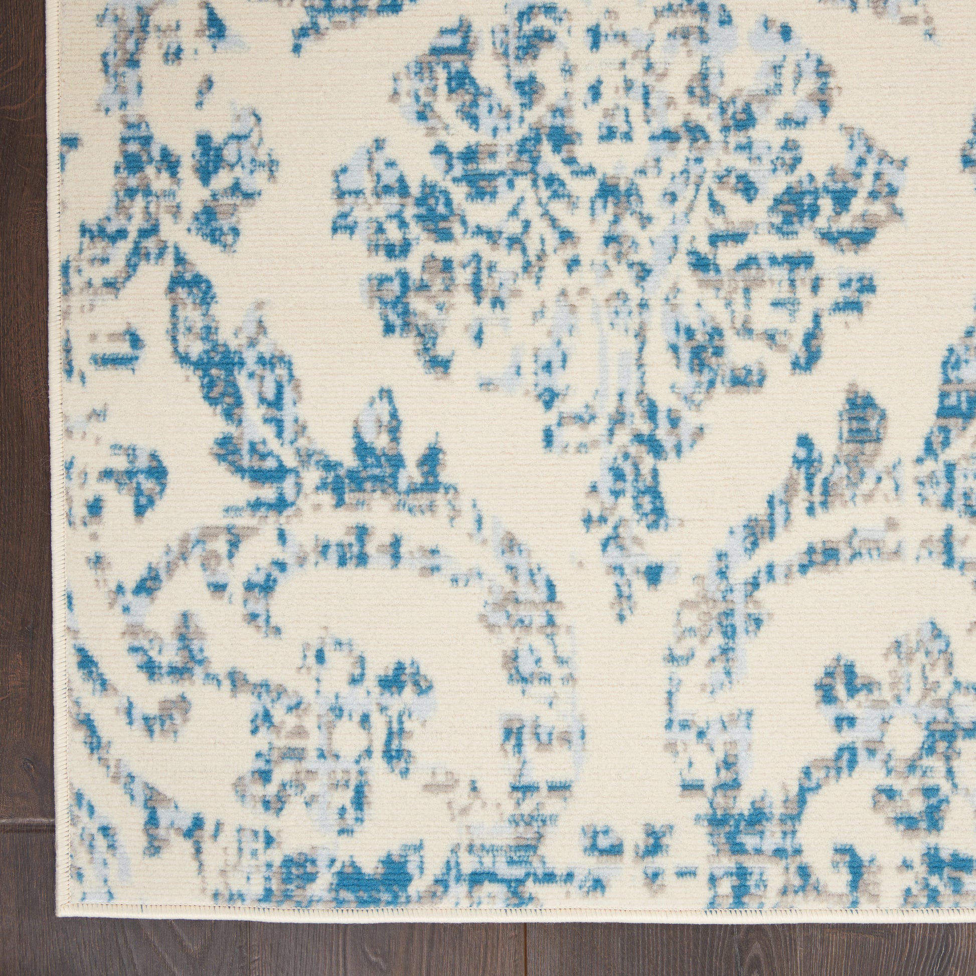 Cream rug with blue damask floral pattern, rectangular shape, with dark wood floor edge visible.