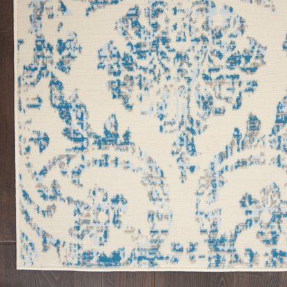 Cream rug with blue damask floral pattern, rectangular shape, with dark wood floor edge visible.