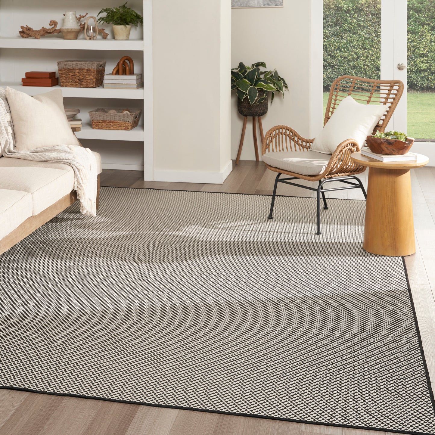 Light gray rectangular woven area rug with subtle geometric pattern and dark border in a modern, cozy living room.