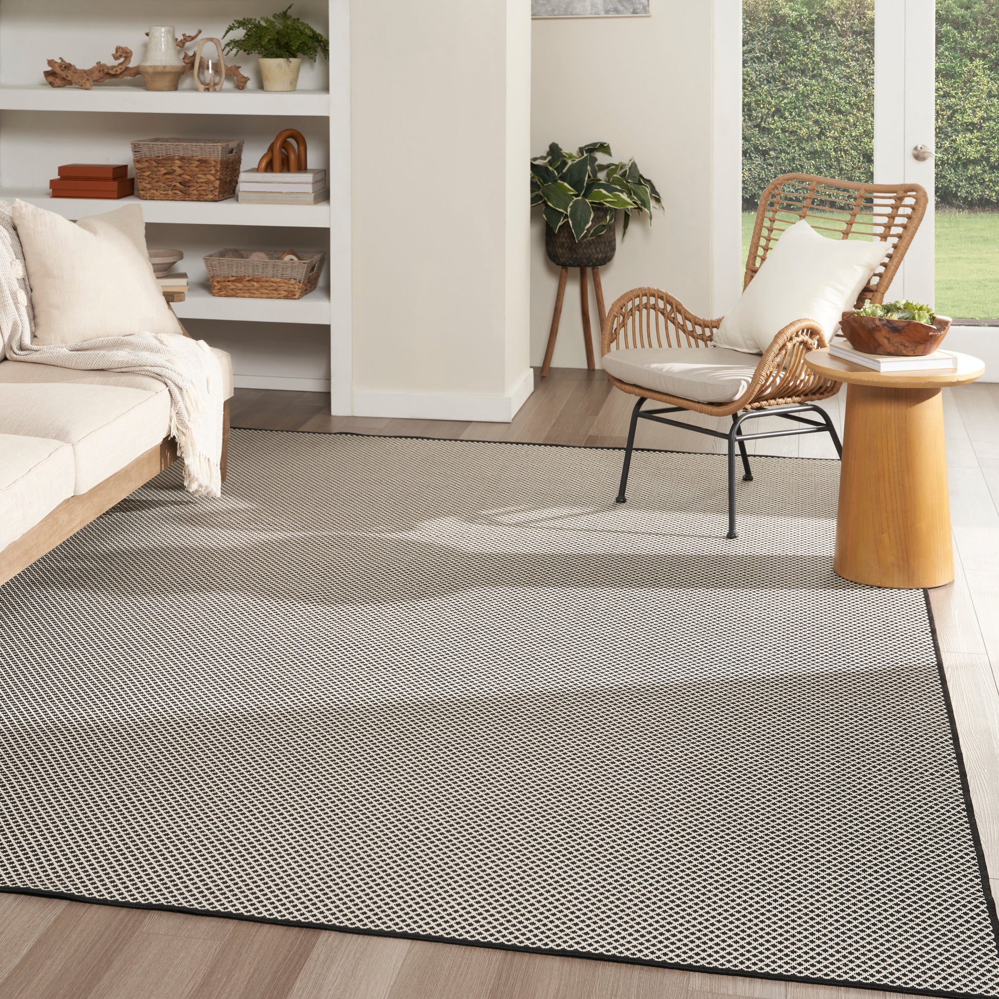 Light gray rectangular woven area rug with subtle geometric pattern and dark border in a modern, cozy living room.