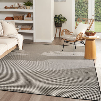 Light gray rectangular woven area rug with subtle geometric pattern and dark border in a modern, cozy living room.