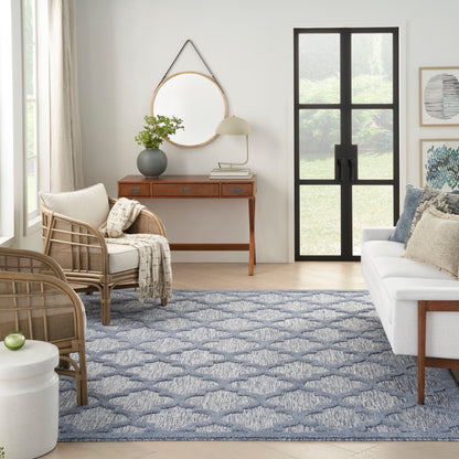 Cozy living room with blue geometric rug, rattan chairs, white sofa, wooden console, round mirror, plant, lamp, glass door.