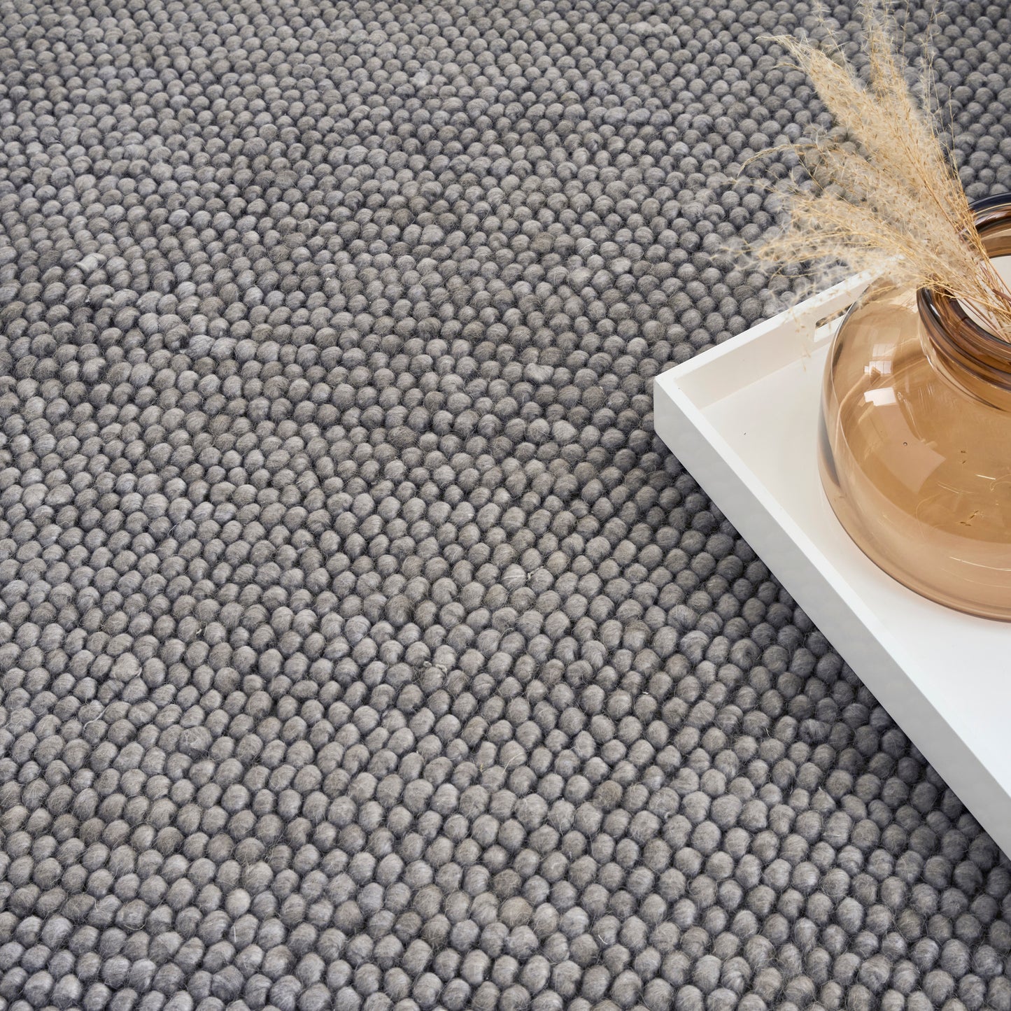 Gray boucle carpet texture, white tray, round amber glass vase & dried pampas grass.