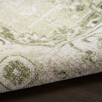 Close-up of a plush green & ivory patterned rug with a rolled edge on dark wood floor.