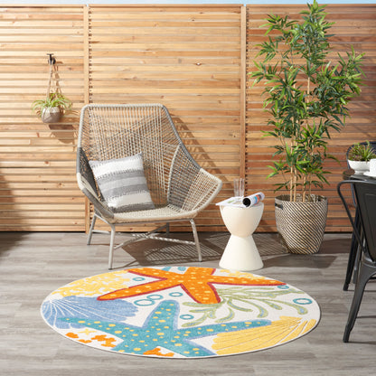 Outdoor lounge with wooden slat fence, wicker armchair, striped cushion, colorful starfish rug, white side table, plants.