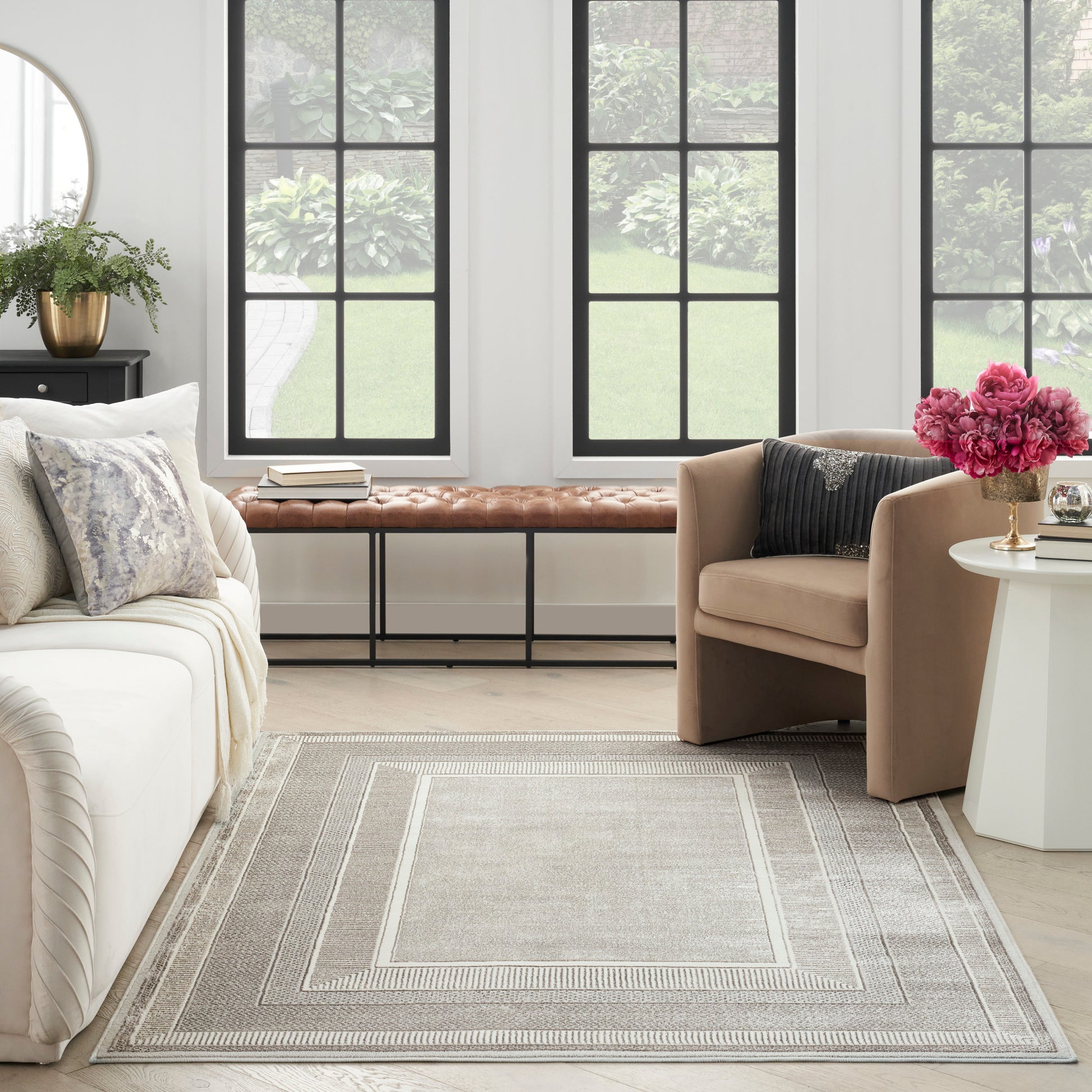 Bright neutral living room with white sofa, beige armchairs, gray geometric rug, brown bench, and pink flowers.
