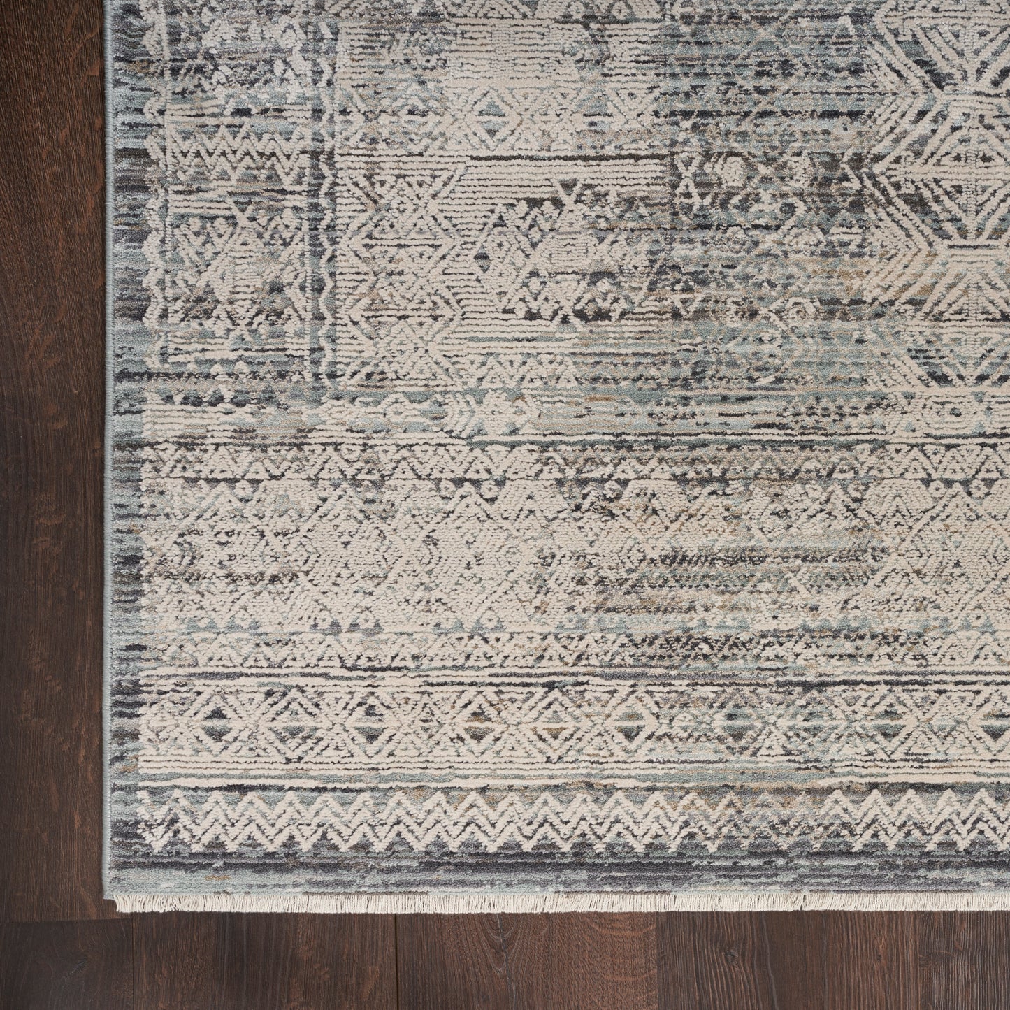 Muted blue and ivory geometric patterned area rug with fringed edge on dark wood floor