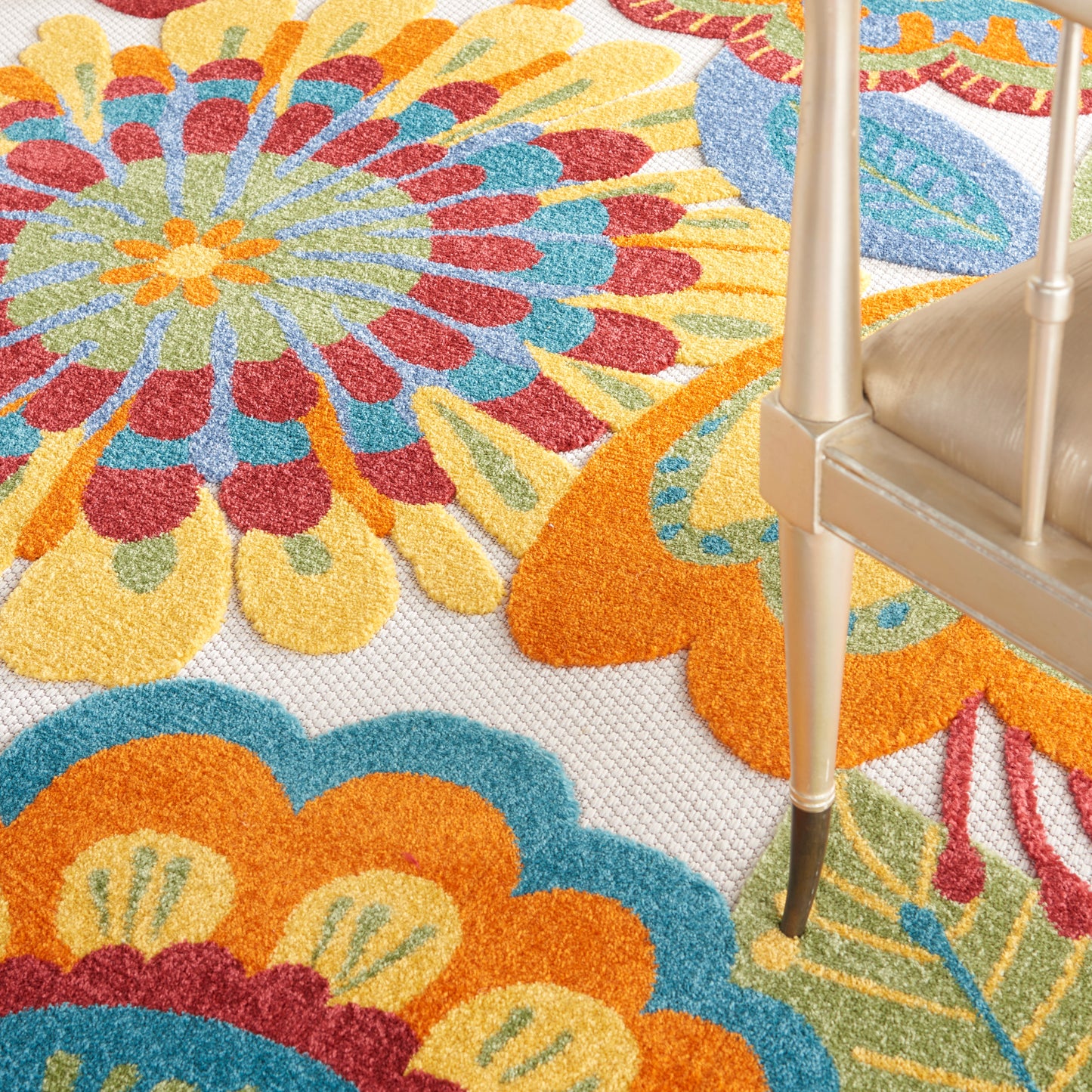 Close-up of a colorful mandala-patterned rug in orange, blue, yellow and red hues; gold chair leg visible.