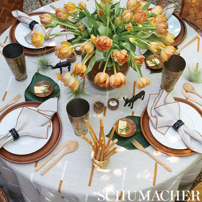 Rustic table setting with orange-yellow tulip centerpiece & brown chargers & white napkins & wooden utensils & brass goblets.